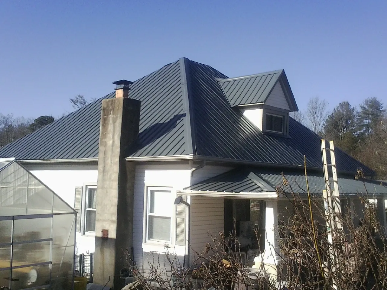 Dark blue standing seam metal roof on a white farmhouse with dormer — Slate & Tile Roof Repair by Roofing Brothers in Standish