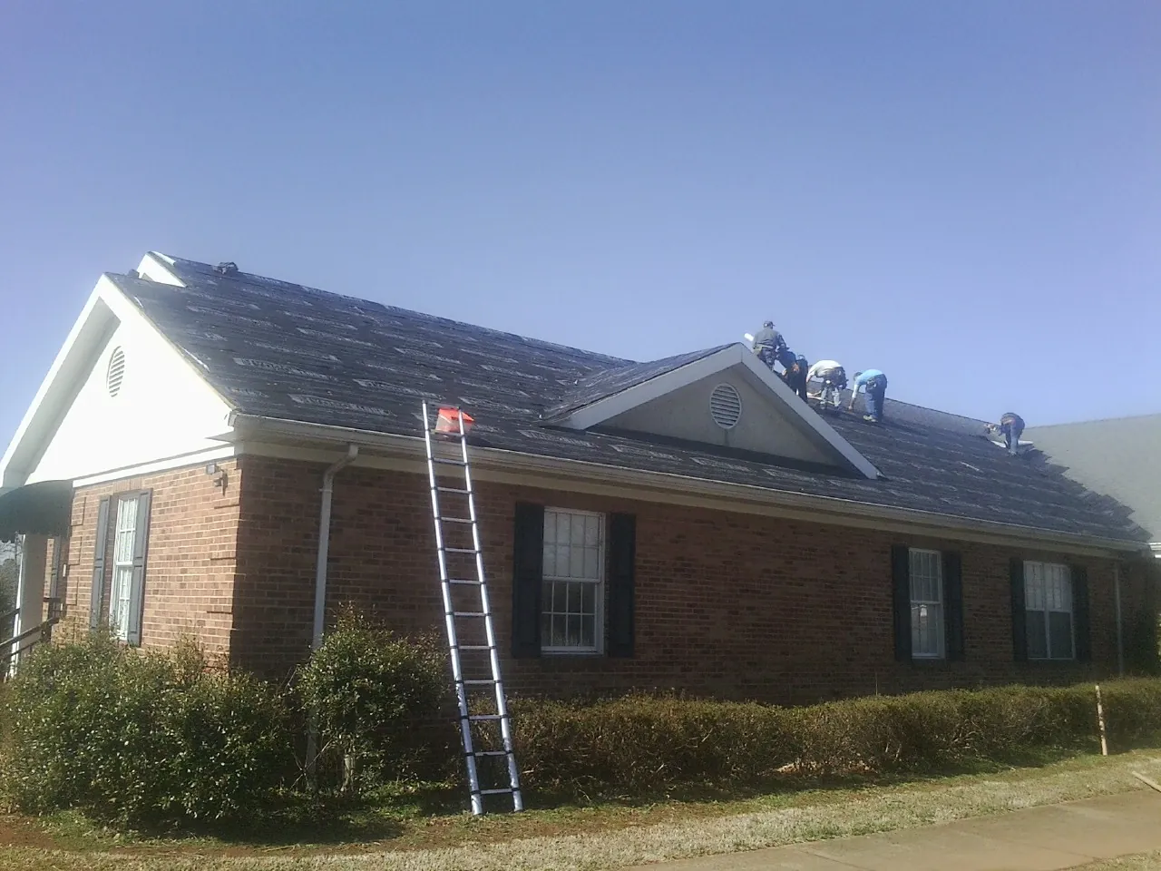 Crew tearing shingles off a brick ranch roof with a ladder set — Emergency Roof Repair work by our crew in Standish