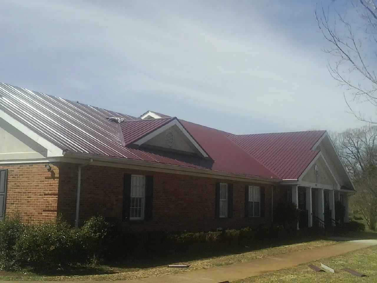 Red metal roof with gabled entries on a long brick building, from a Hail Damage Roof Repair job in Standish