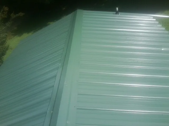 New green metal panels meeting at the ridge of a roof — Flat Roof Repair work by our crew in Standish