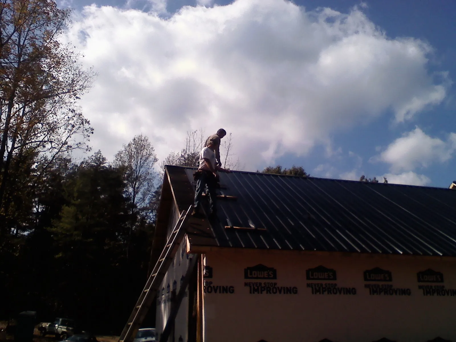 Roofer fastening dark metal panels high against a cloudy sky, from a Roof Inspection job in Standish