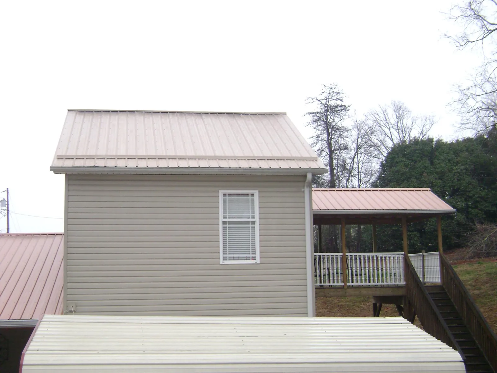 Tan metal roofs on a two story addition and attached porch, from a Roof Replacement job in Standish